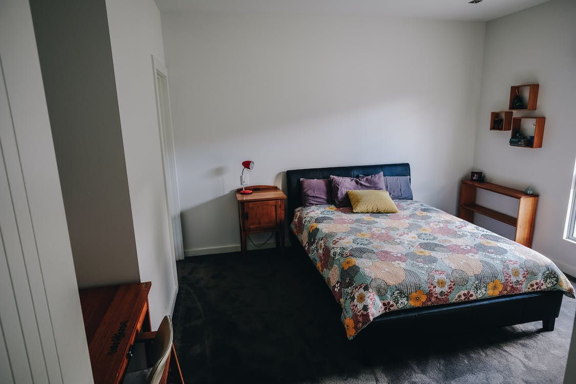 cozy bed and wooden nightstand with shelves in light bedroom