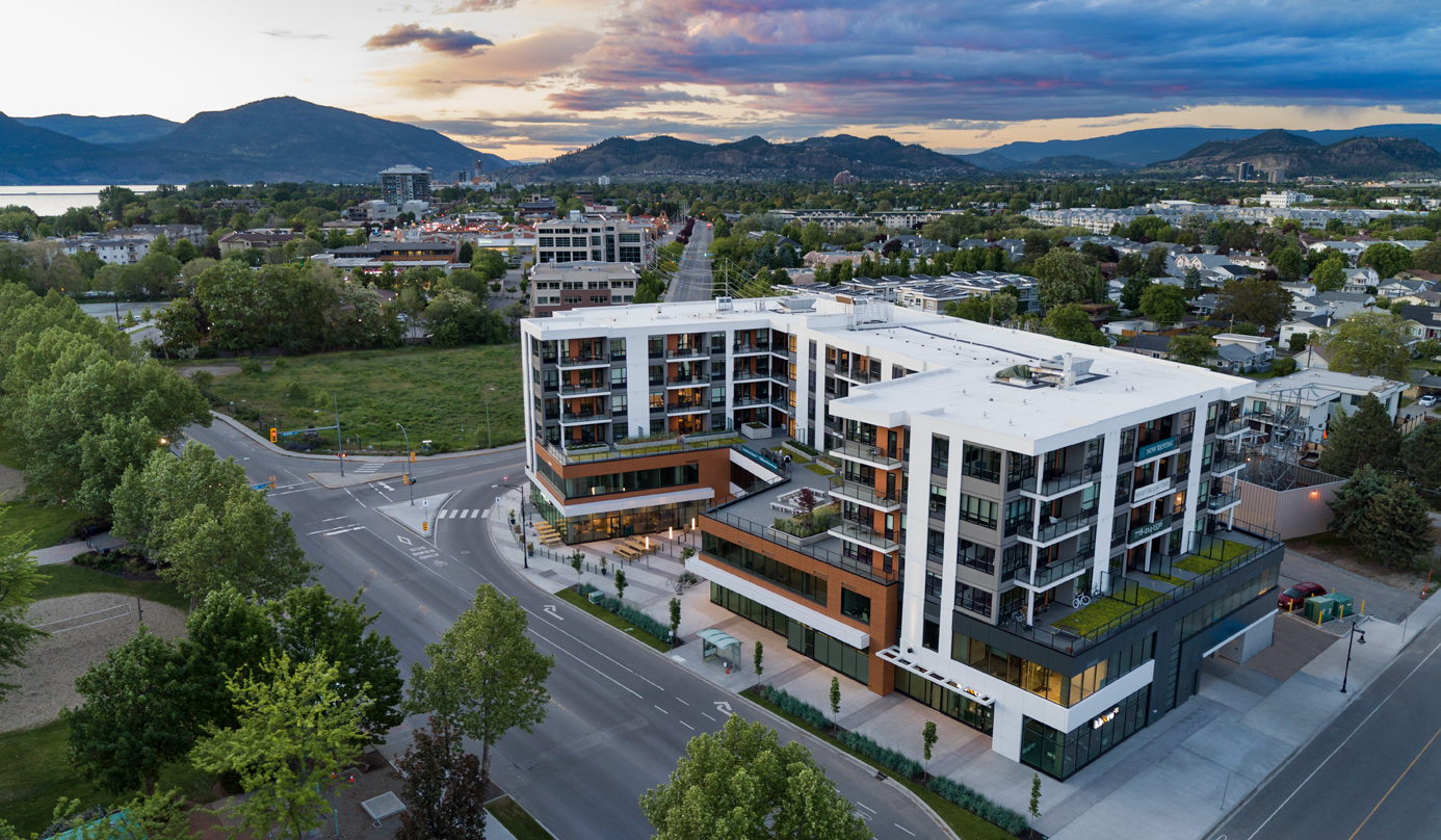 The Shore Kelowna exterior with Lakeshore road in the foreground along with gyro beach's volleyball courts, and the city of kelowna in the background