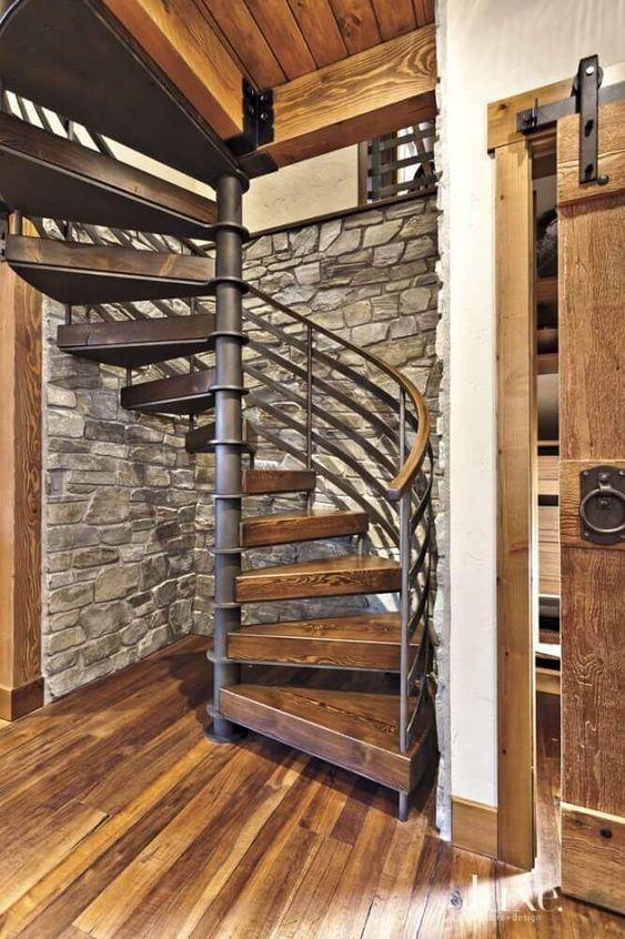 Ambiente rústico com escada caracol de ferro com degraus de madeira rústica para harmonizar com a decoração e corrimão preto.