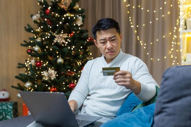 Upset christmas man with laptop trying to make online purchase in online store asian man holding