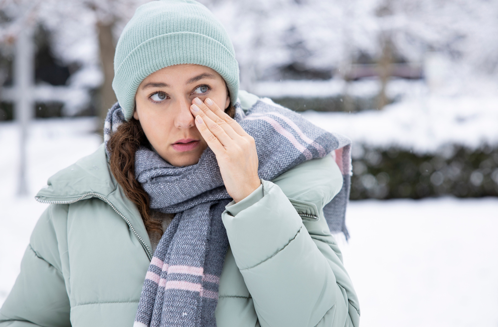 a woman walking outside in the winter rubs her eyes, concerned that her contacts have frozen