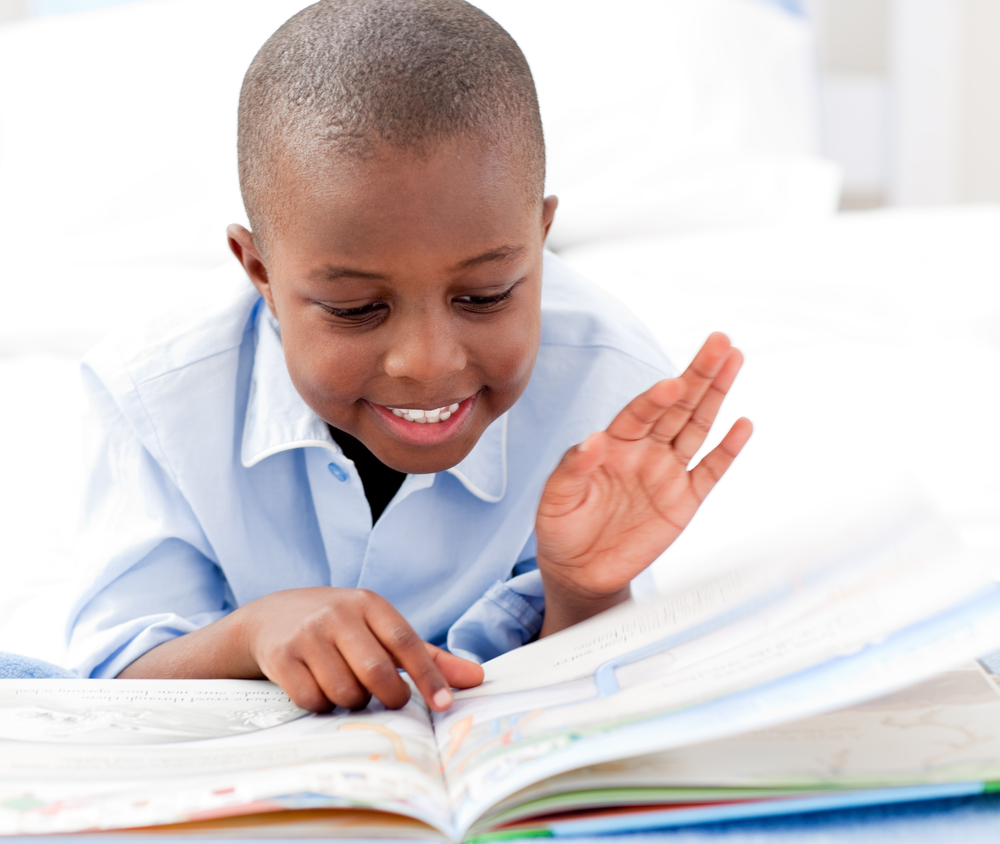 Happy boy reading a book on his bed