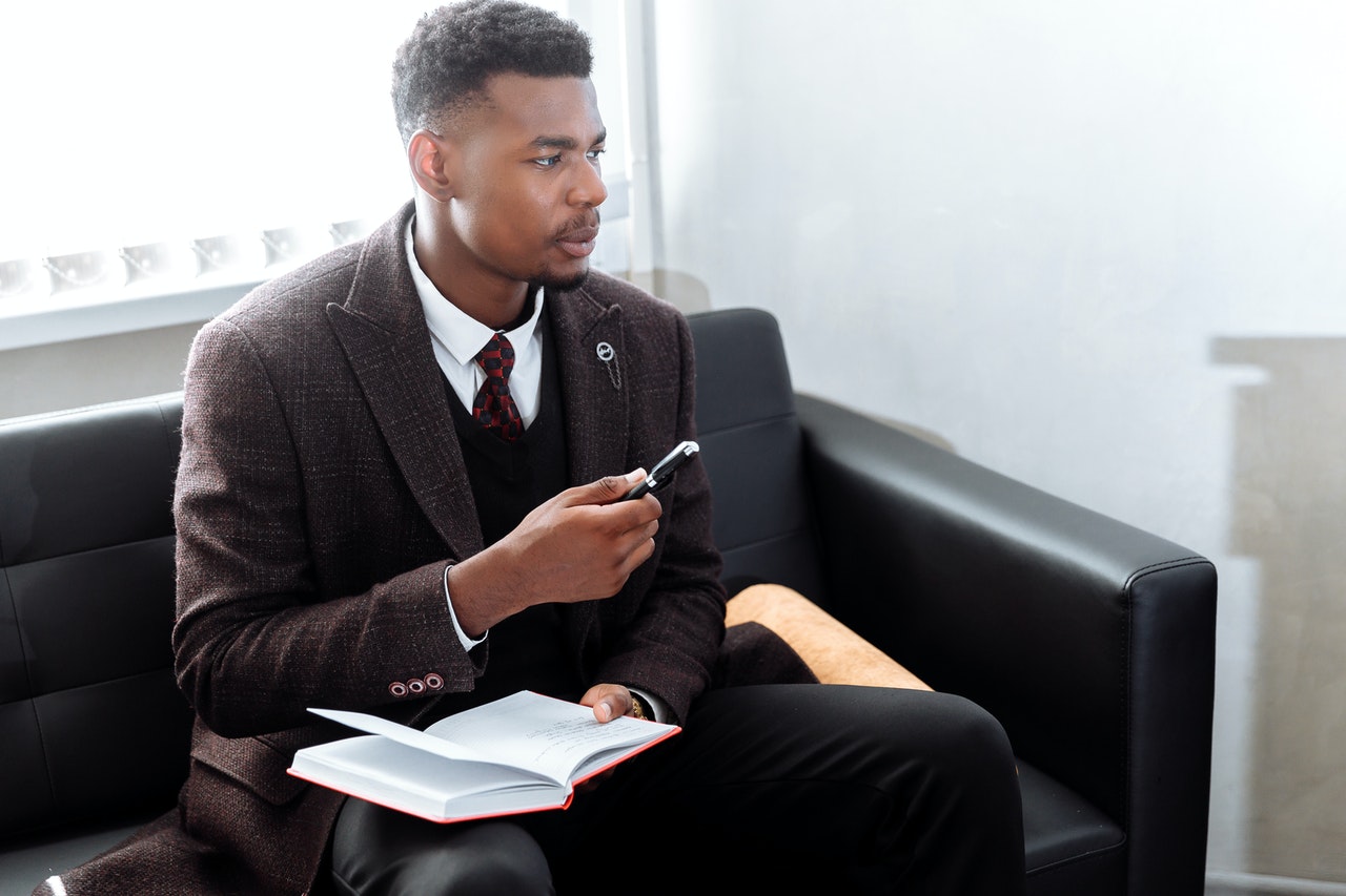 Man in a brown suit sitting on a leather couch waiting for an interview at Goldman Sachs.