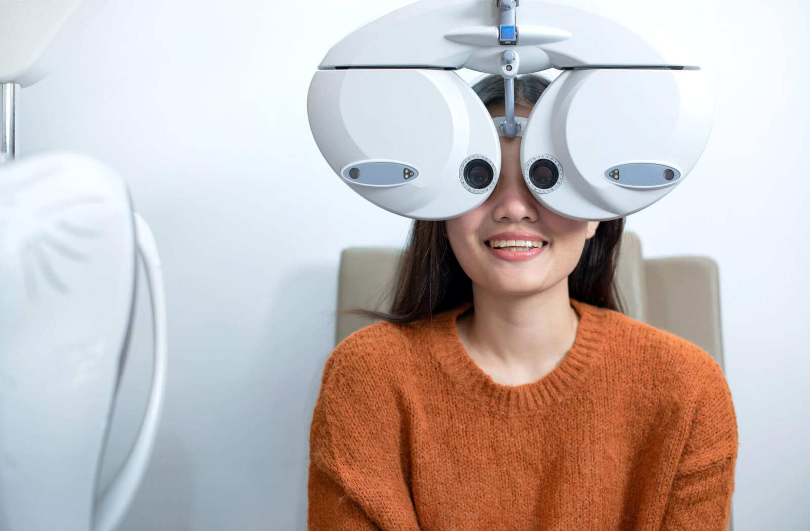 A woman in an optometrist's office looking through a device that determines her eyeglass prescription and tests her vision.