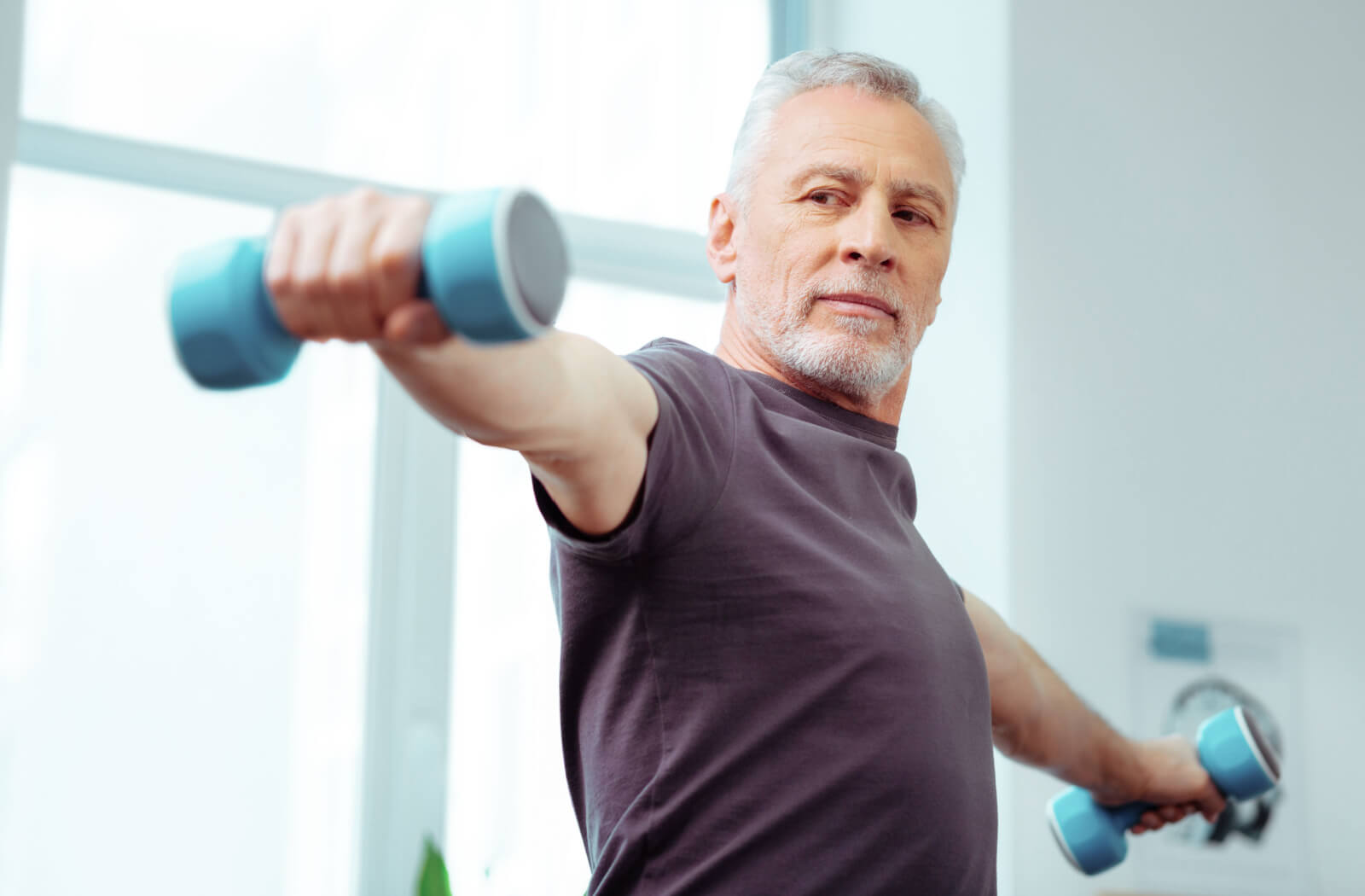 A senior man holding his arms out to his sides with a small dumbbell in each hand.