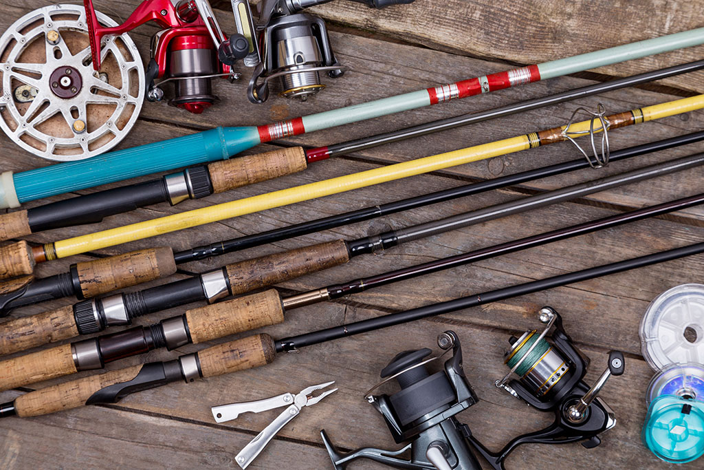 Fishing rods and a few reels lie on a wooden table
