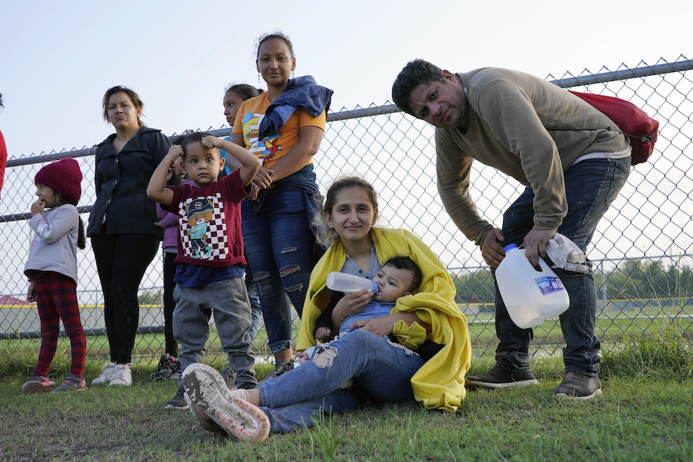 A group of migrant children and parents in a grassy setting.