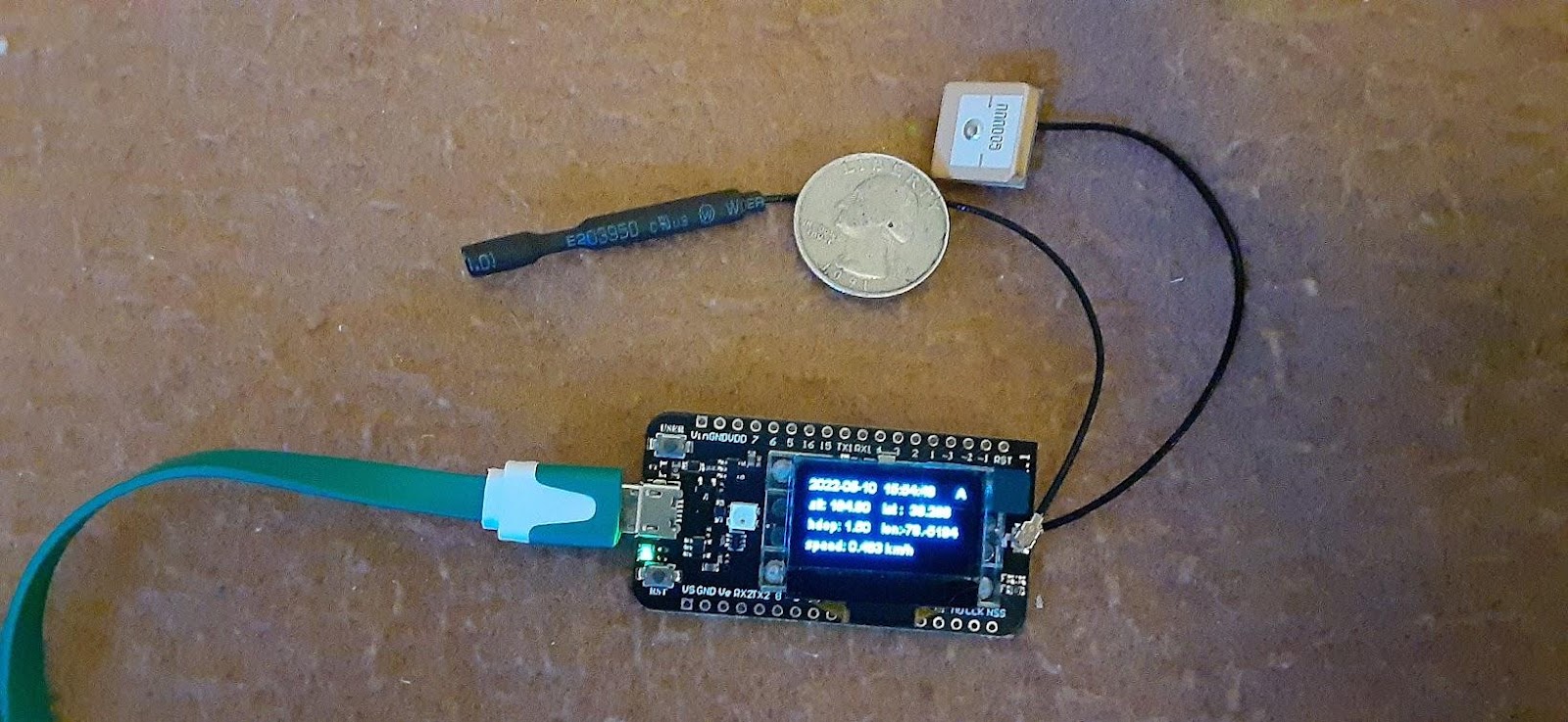 A green cable connects a motherboard to two sensors, one square and one cylindrical. The whole apparatus is about as big as a two quarters. 