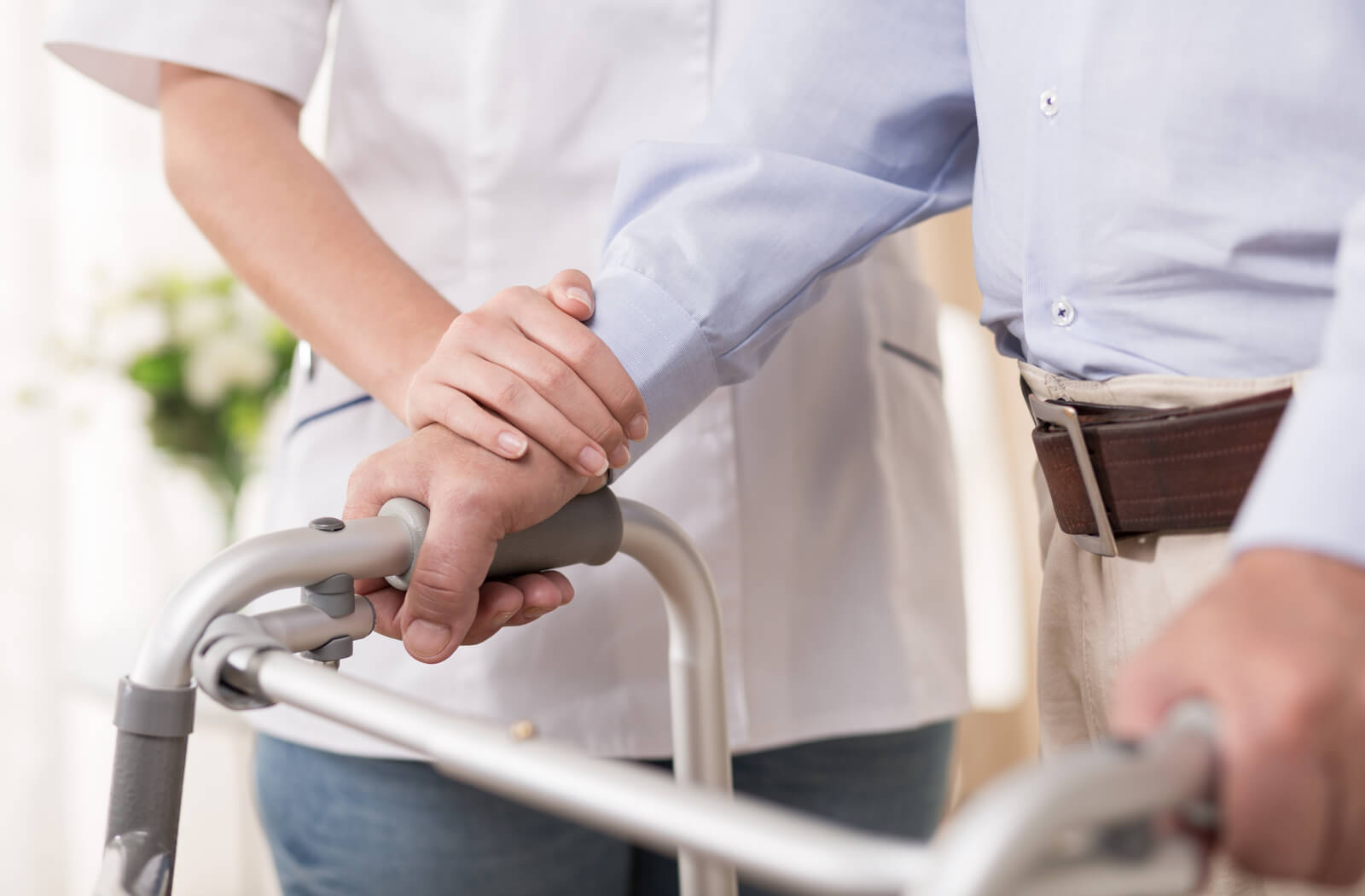 A close-up image of a man holding a walker, while a nurse supports his arm.