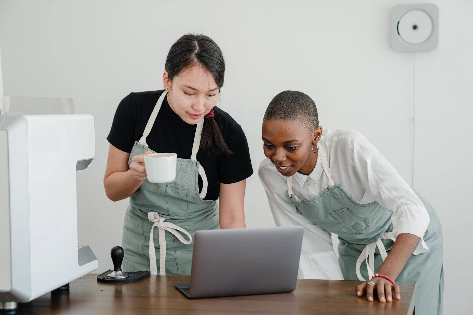 two women, one with a coffee cup, looking at a laptop screen