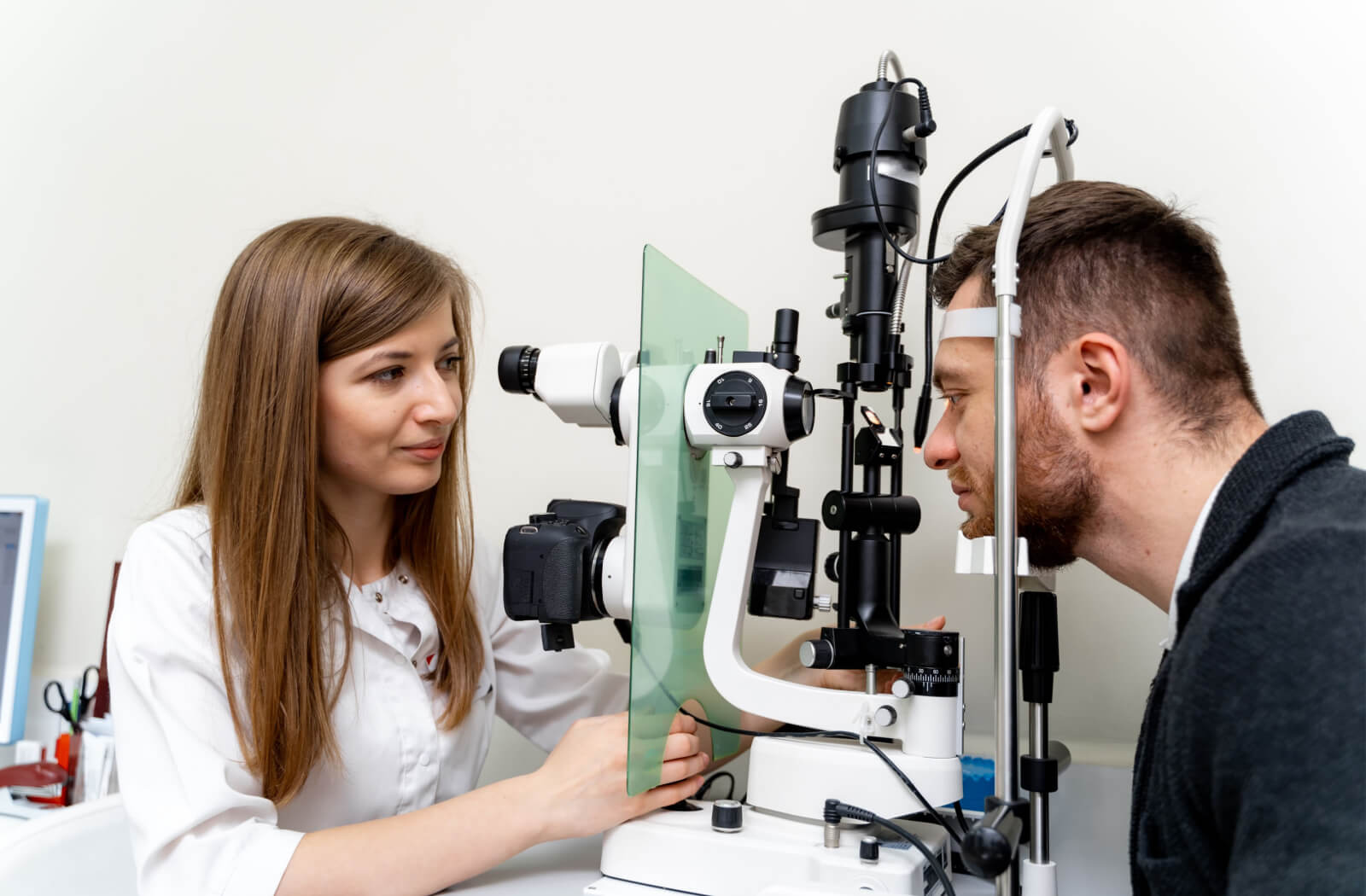 A man looking into a piece of optometry equipment as his female optometrist performs an eye exam.