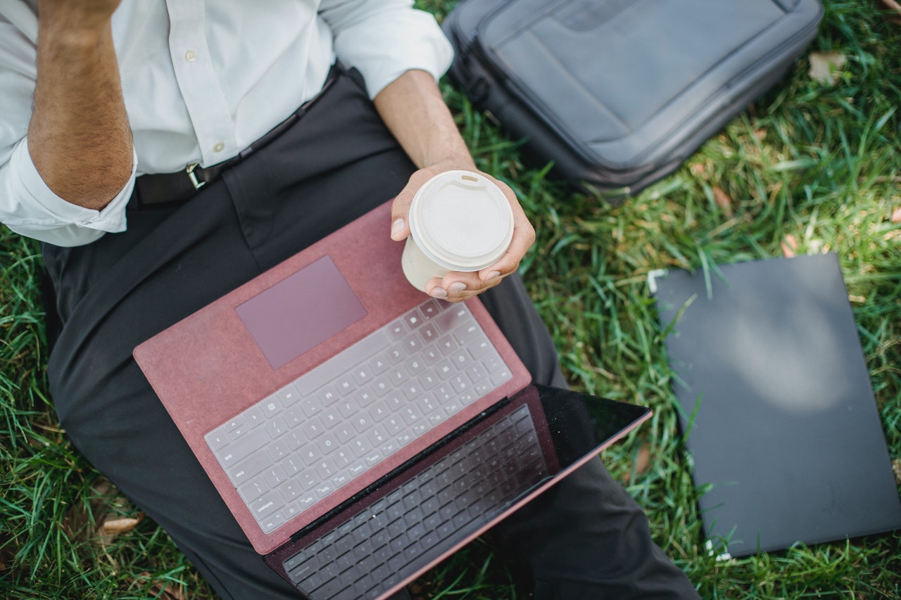 Persona afuera con una taza de café para llevar y su computadora portátil en el regazo