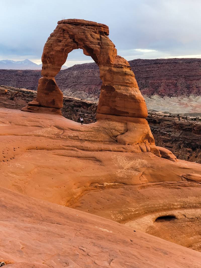 A woman standing under Delicate Arch at Arches National Park, a great winter choice when you’re considering the best national parks to visit by month