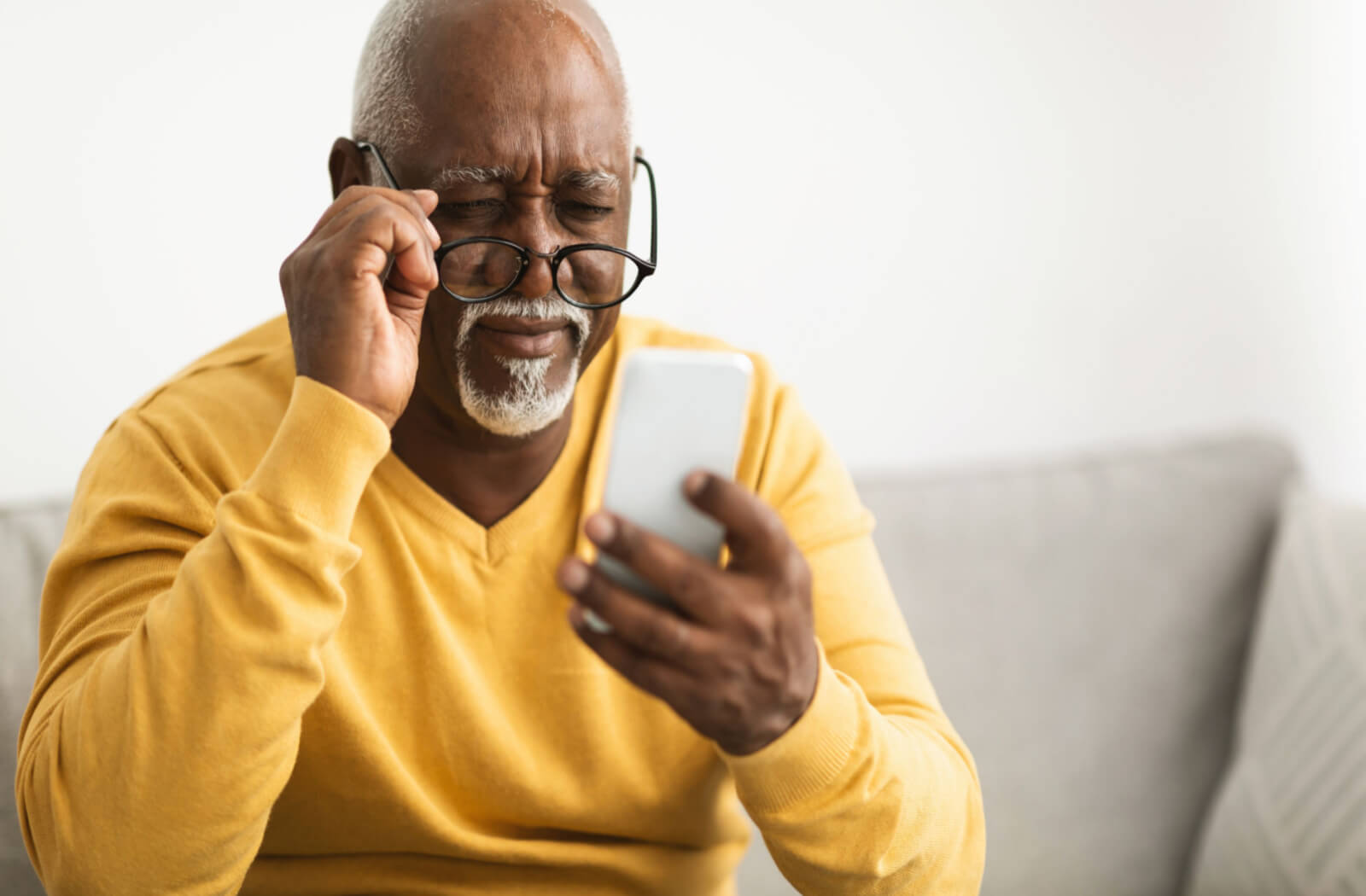 a man looks over the top of his glasses at his cellphone because he is experiencing blurred vision due to glaucoma