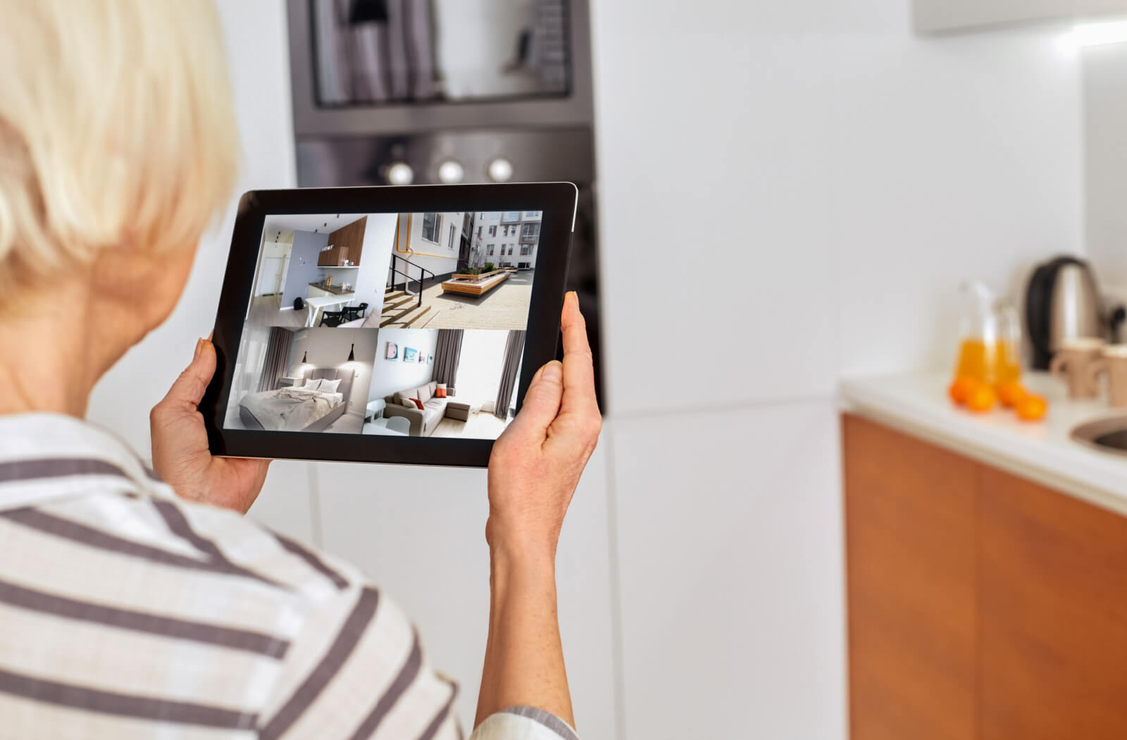 A senior woman in a striped shirt checking surveillance cameras using her tablet.