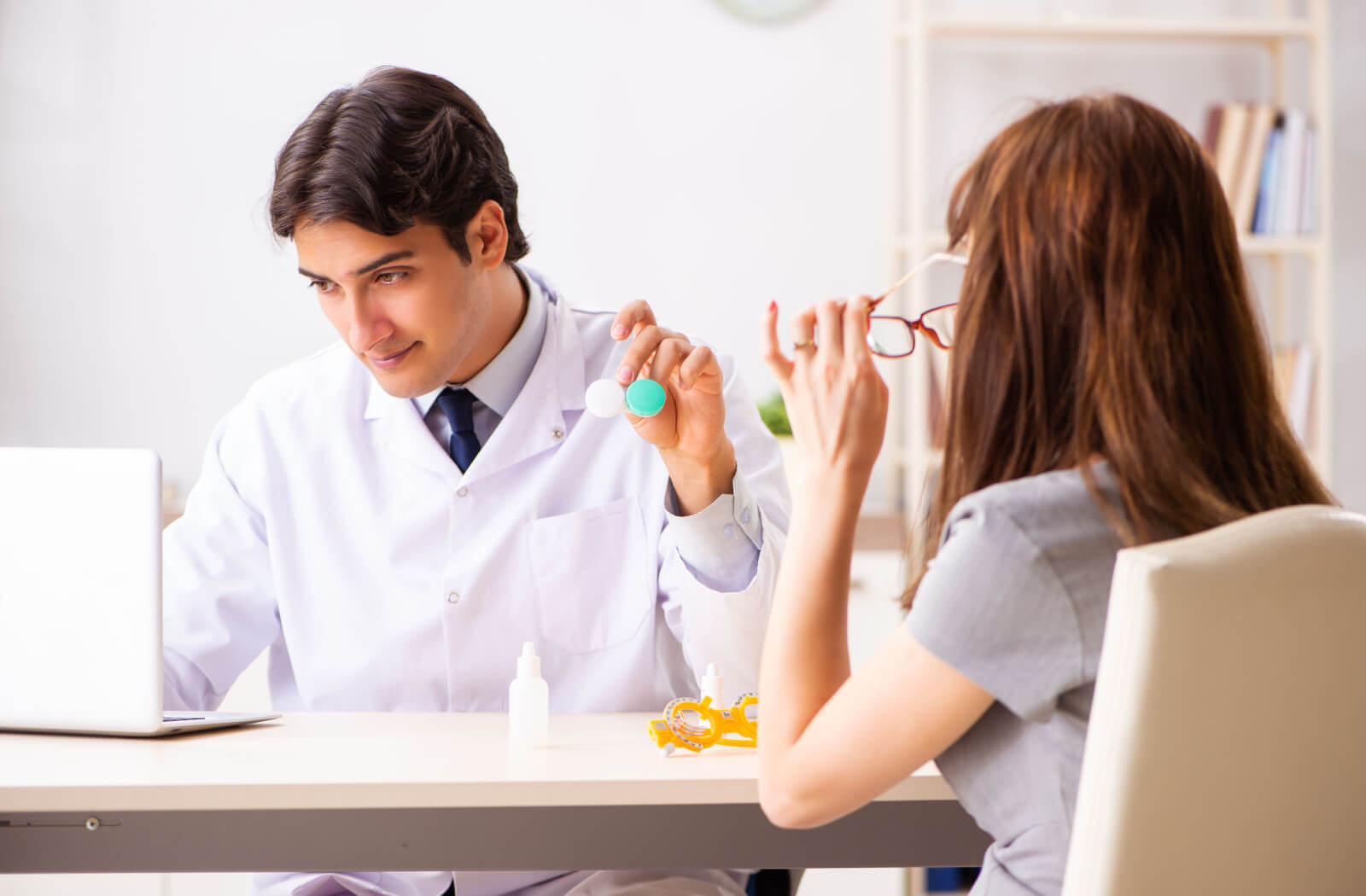 an optometrist hands his patient a contact lens case while analyzing her automated patient file