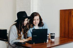 Two women sitting at a table in a diner and researching ways for painting contractors to keep busy in winter on a laptop