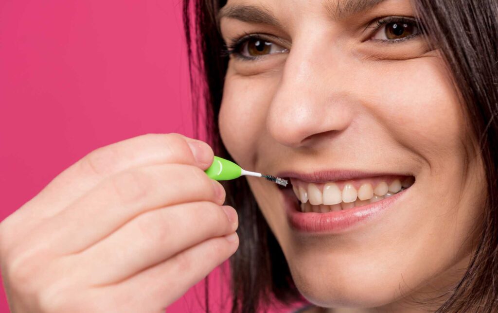 06 A smiling woman cleaning her teeth with an interdental or interproximal brush.