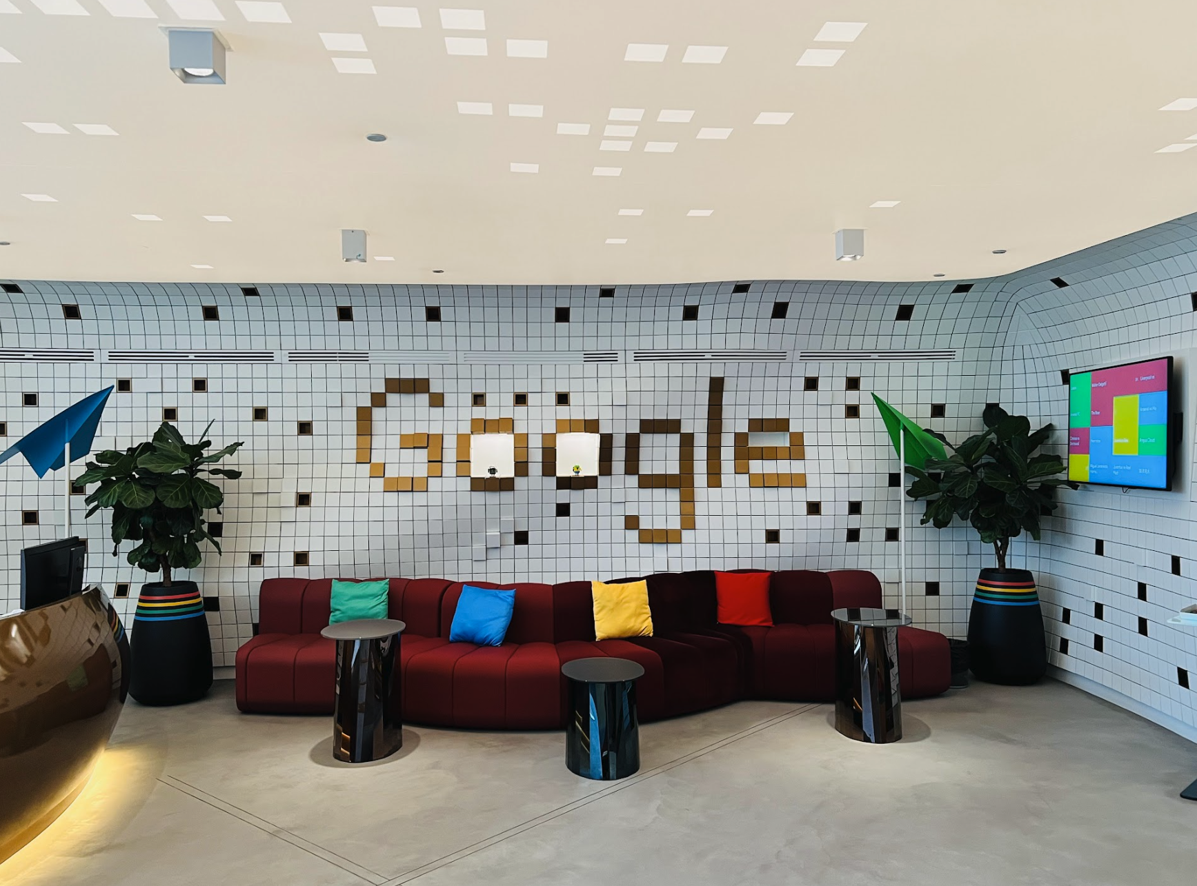구글 두바이 오피스에 빨간 쇼파와 3개의 검은 탁자가  리셉션 공간에 놓여져 있는 모습. 물결 모양 벽에 타일로 구글이라는 단어가 쓰여져 있는 모습.