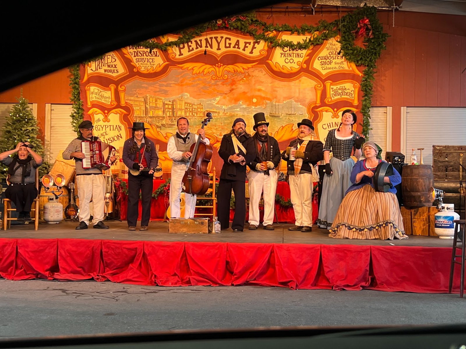 A group of people dressed in 19th century English attire perform on stage.