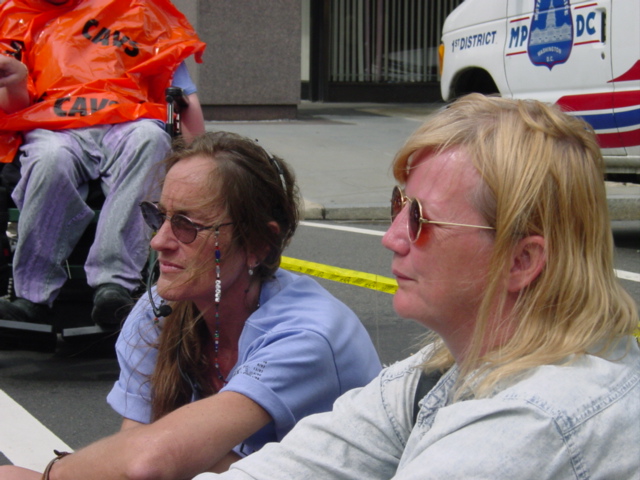 Two women wearing sunglasses sit in the street.