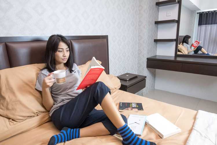 Girl relaxing on a bed with a cup of tea and a book. Importance Of A Mental Health Day