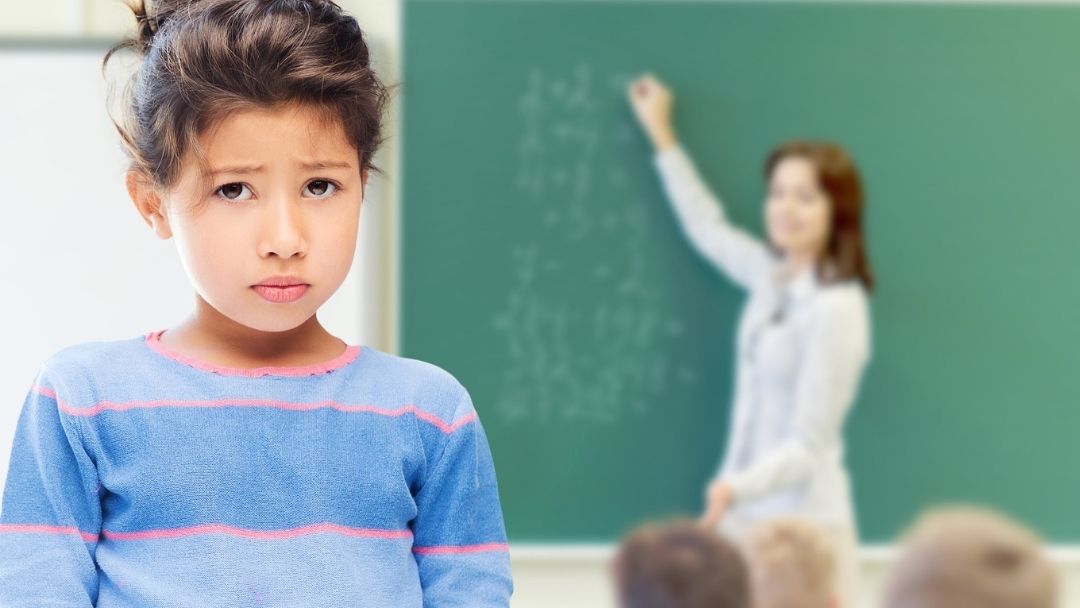 sad little girl getting in trouble at school with teacher in background