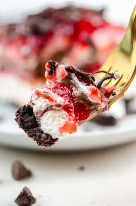 A bite of Oreo crust, cheesecake, strawberries, chocolate pudding, and whipped cream.