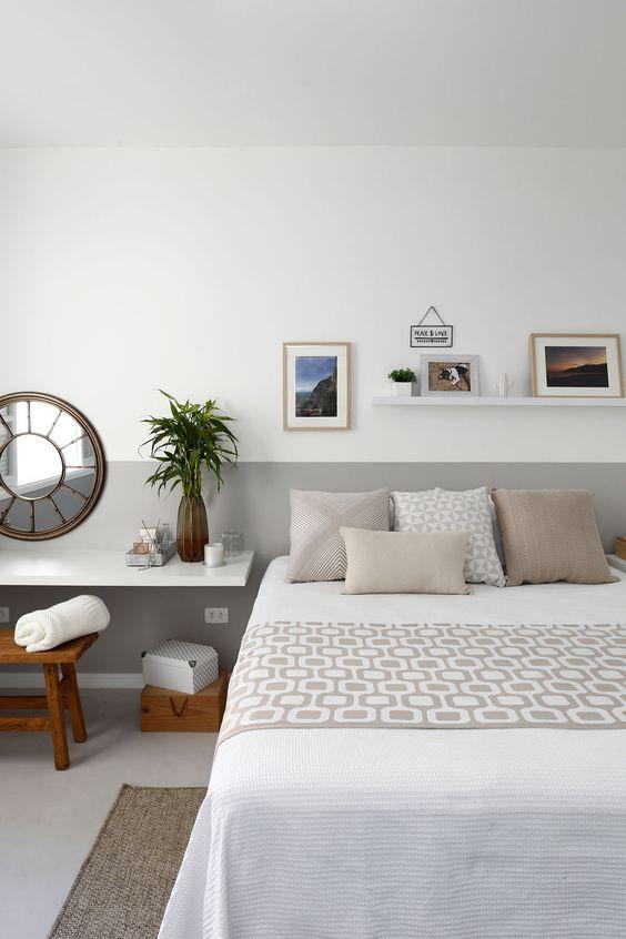 Quarto com cama de casal e parede com técnica de pintura meia parede branca e cinza, quadros decorativos e piso porcelanato branco.