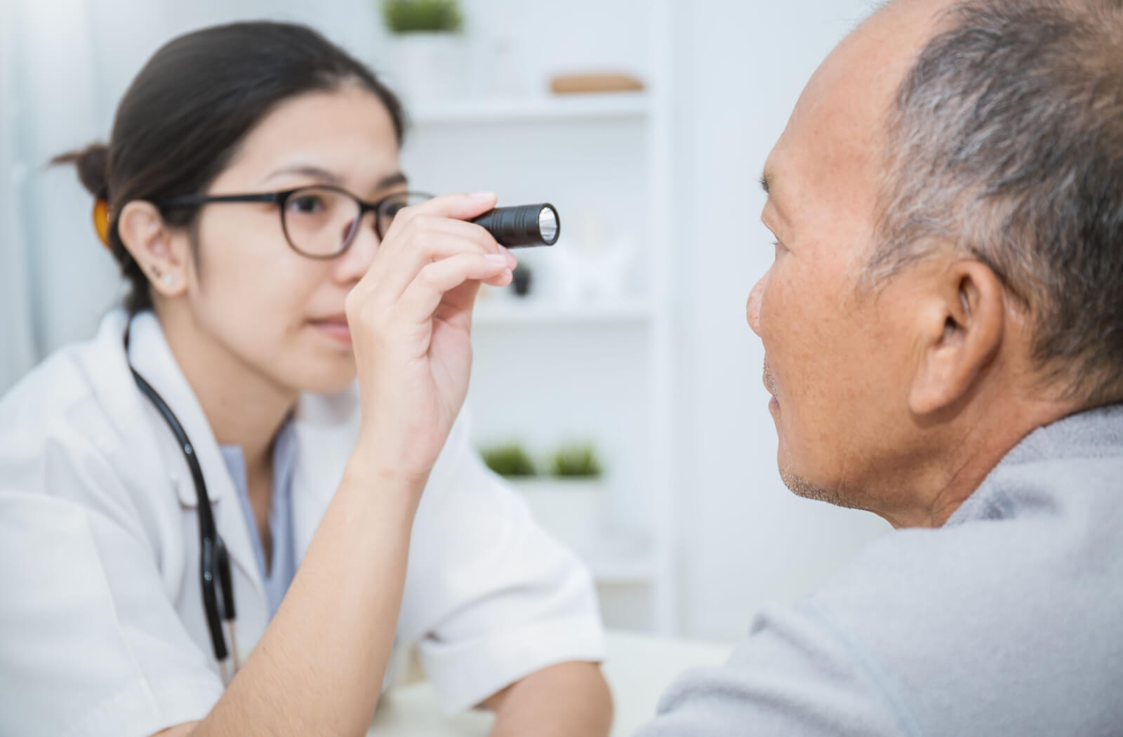 A senior man facing his optometrist as she shines a small flashlight into his eye