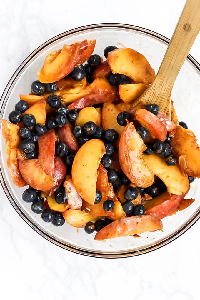 A bowl of sliced peaches and blueberries macerating in sugar and tapioca starch to form the filling for a vegan cobbler