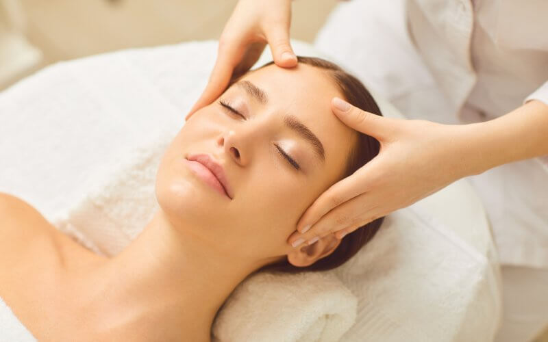 Kỹ thuật viên massage đầu trong lúc chăm sóc da mặt để cải thiện giấc ngủ