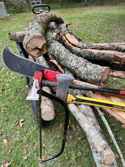 A stack of wood with a axe and a saw

Description automatically generated with medium confidence