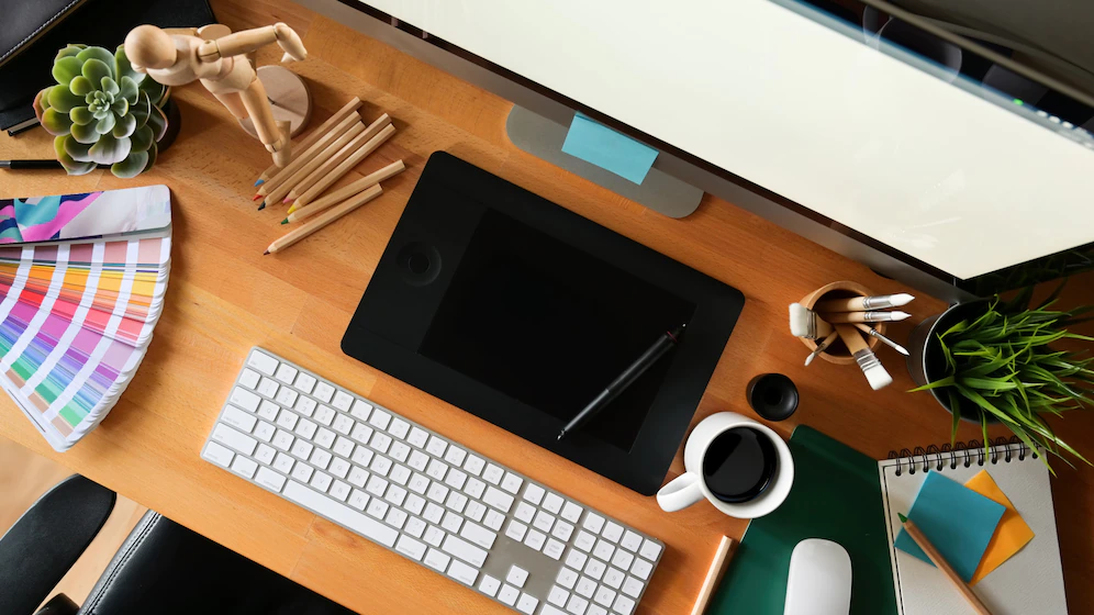 mesa de trabalho de um desenhista, com teclado e tela de computador, mesa digitalizadora, paleta de cores e modelo para desenho.