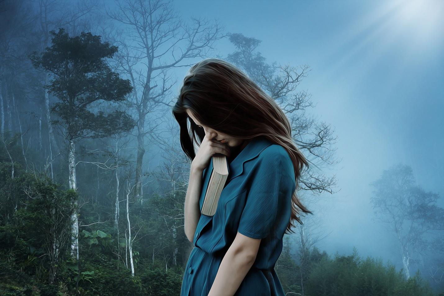 A girl standing with a book alone in the woods