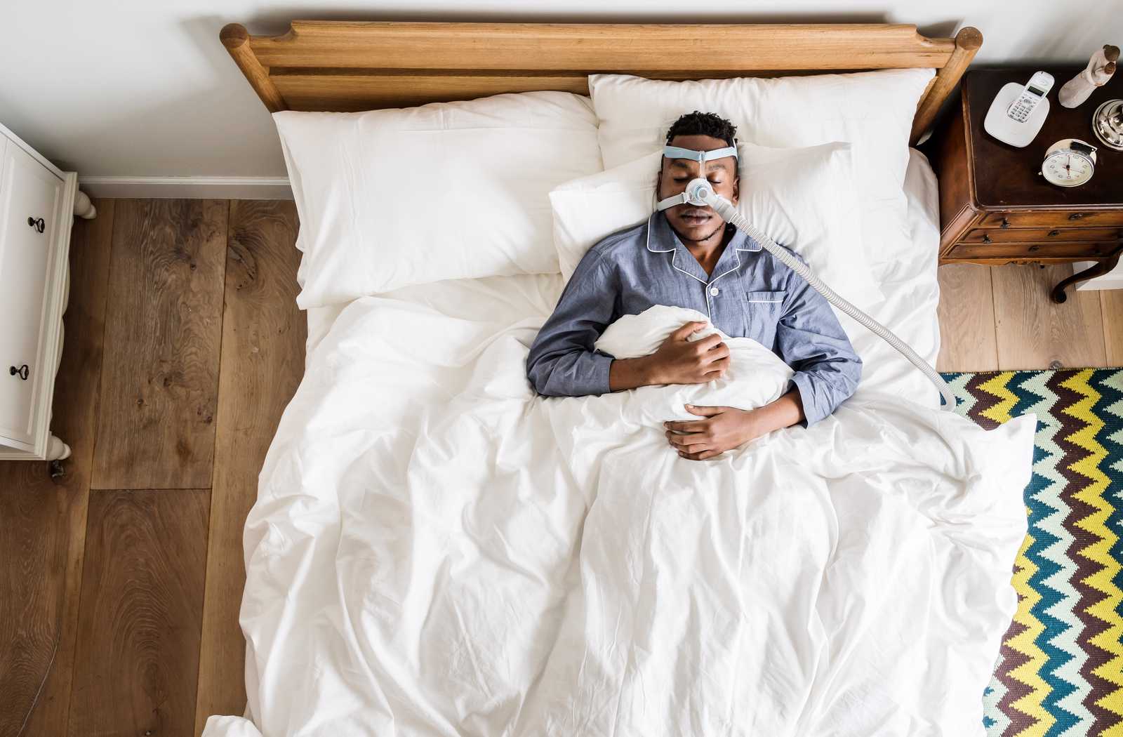 man wearing anti-snoring mask on white sheets with cool filtered lighting