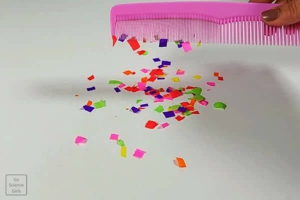 confetti paper scattered on a white surface and a woman's hand holding a pink comb over the confetti.