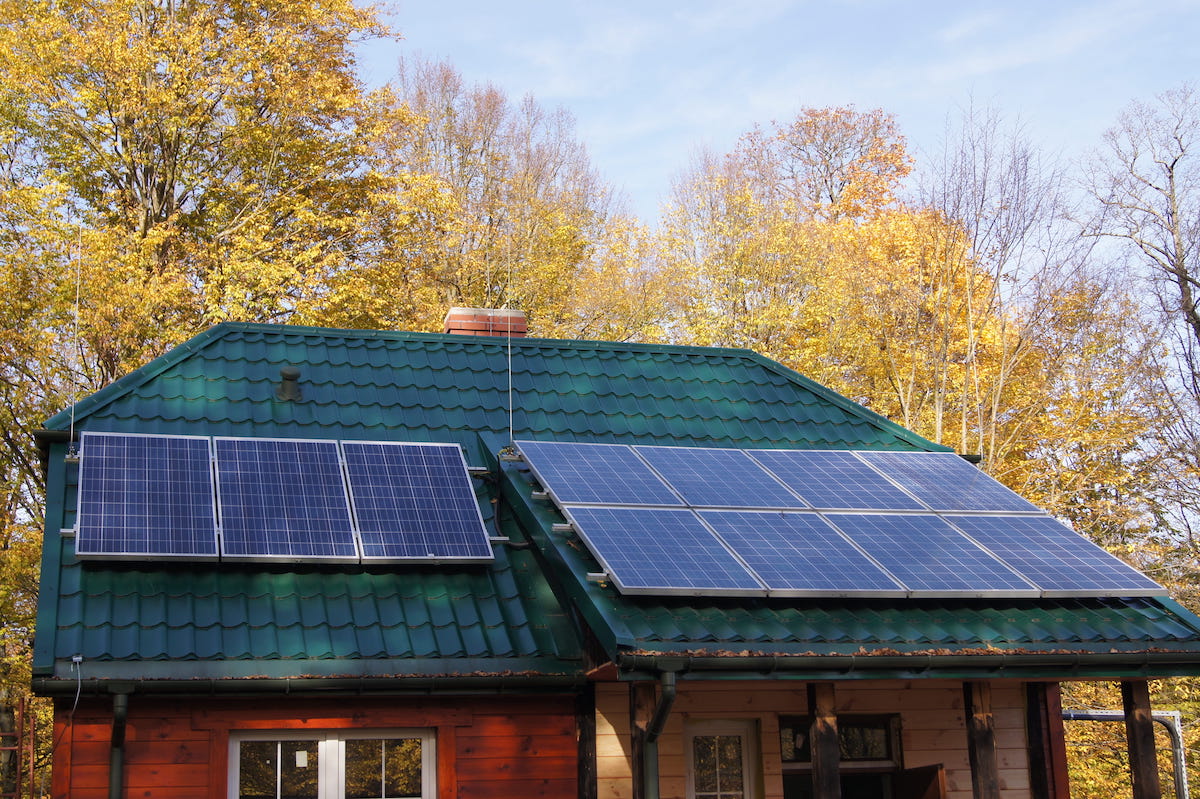 drevený dom so zelenou strechou, na ktorej sú umiestnené solárne panely