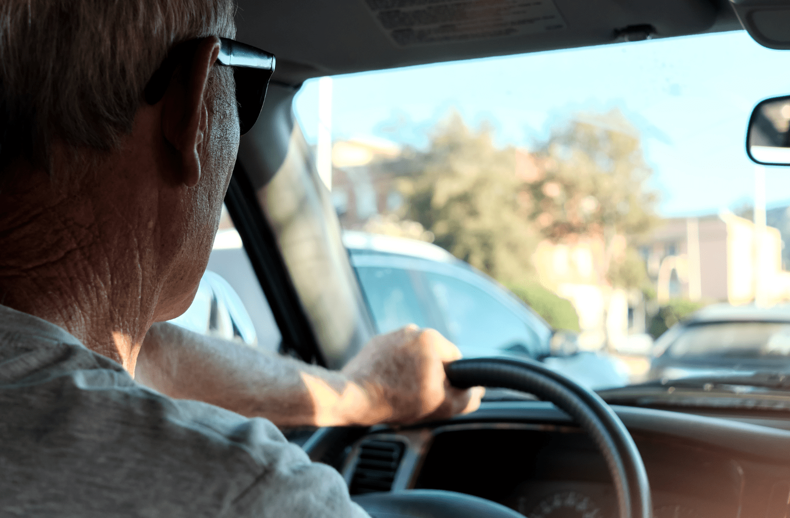 An older man driving a car in the city, traffic around him