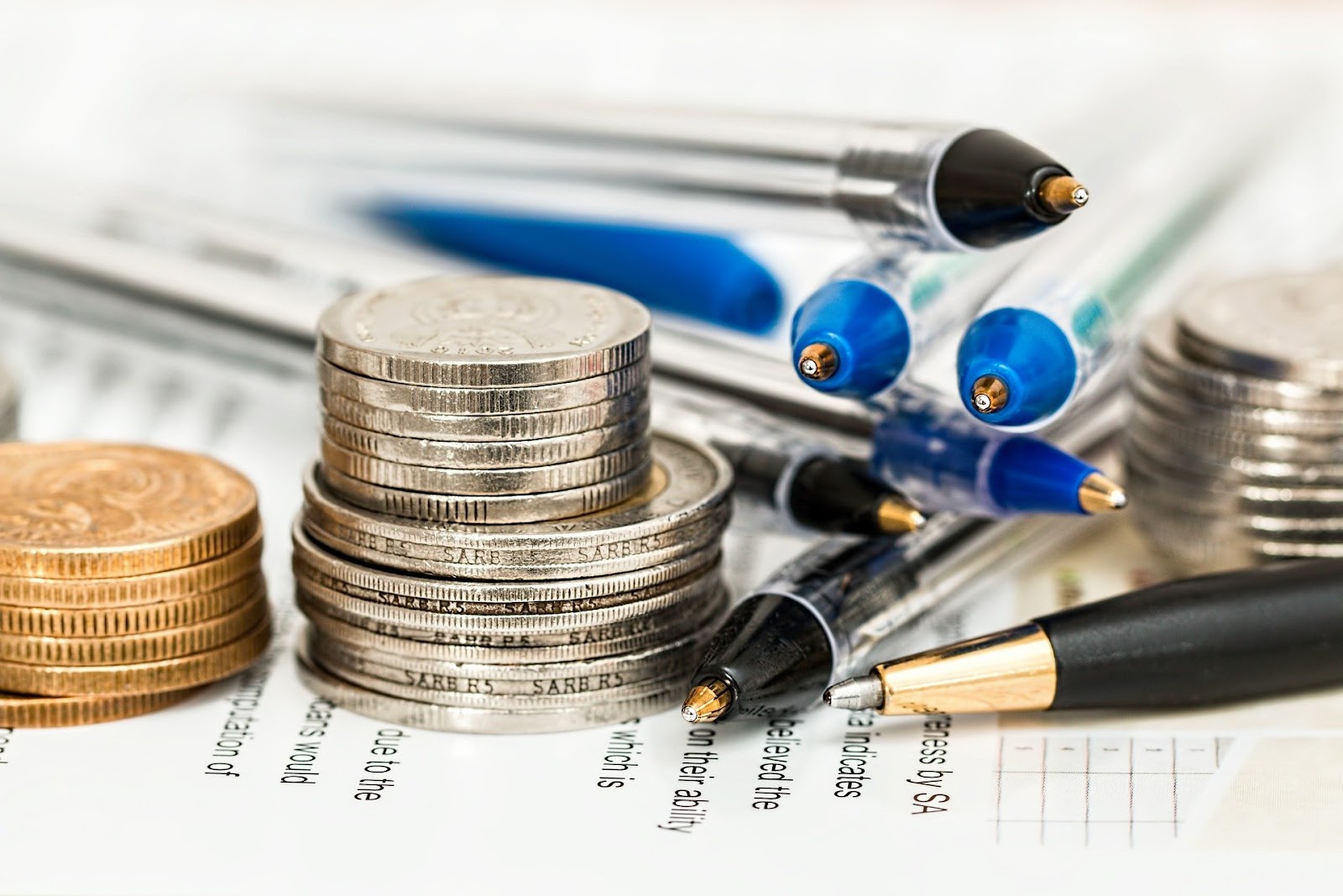 Stacks of coins and several writing instruments sit on a piece of paper.