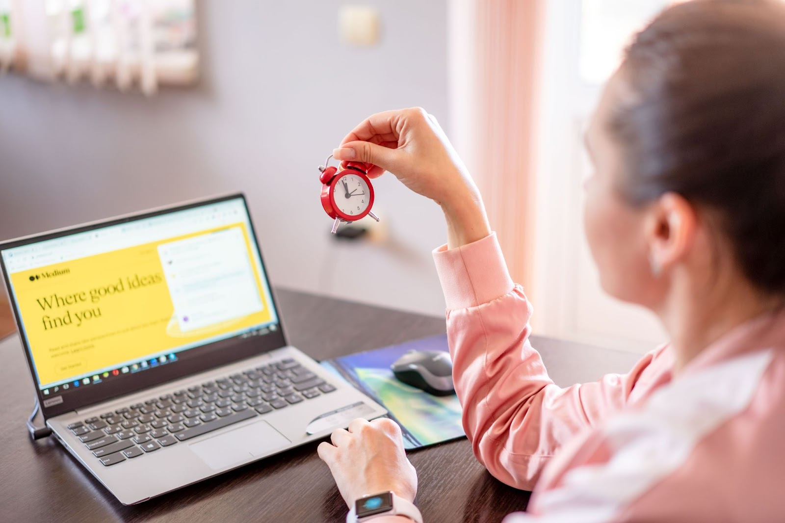 Photo of a woman holding a small red clock while her laptop is open on a yellow screen reading 'Where good ideas find you'