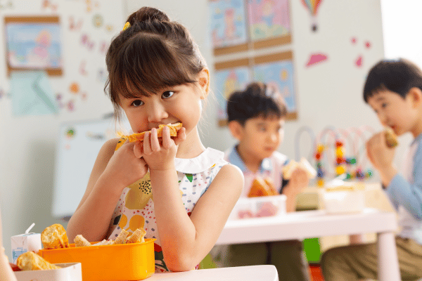 young girl eating a sandwich at a table at school