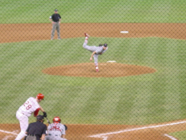 Pitcher with follow-through raises his leg above his head. The batter is in mid swing. 