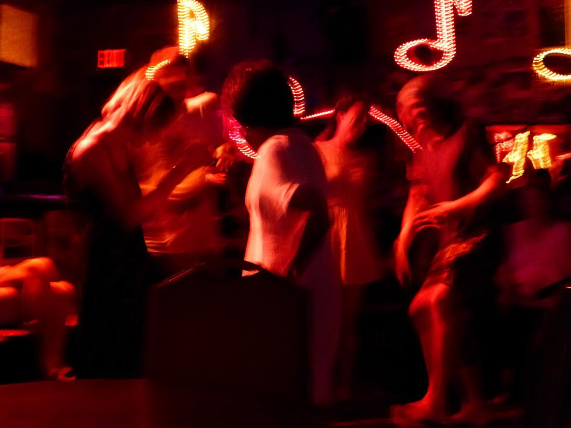 Dancers move and revel under red light in a decorated nightclub.