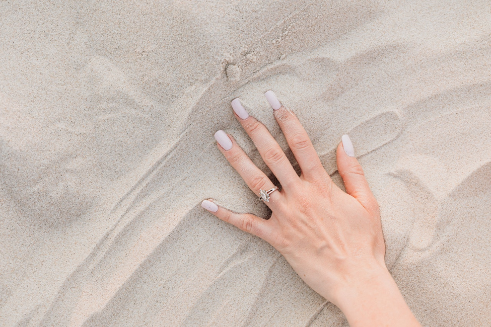 A hang of a woman with white nails and a ring on sand