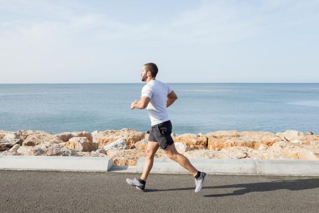 Young strong sporty man running on road along sea Free Photo