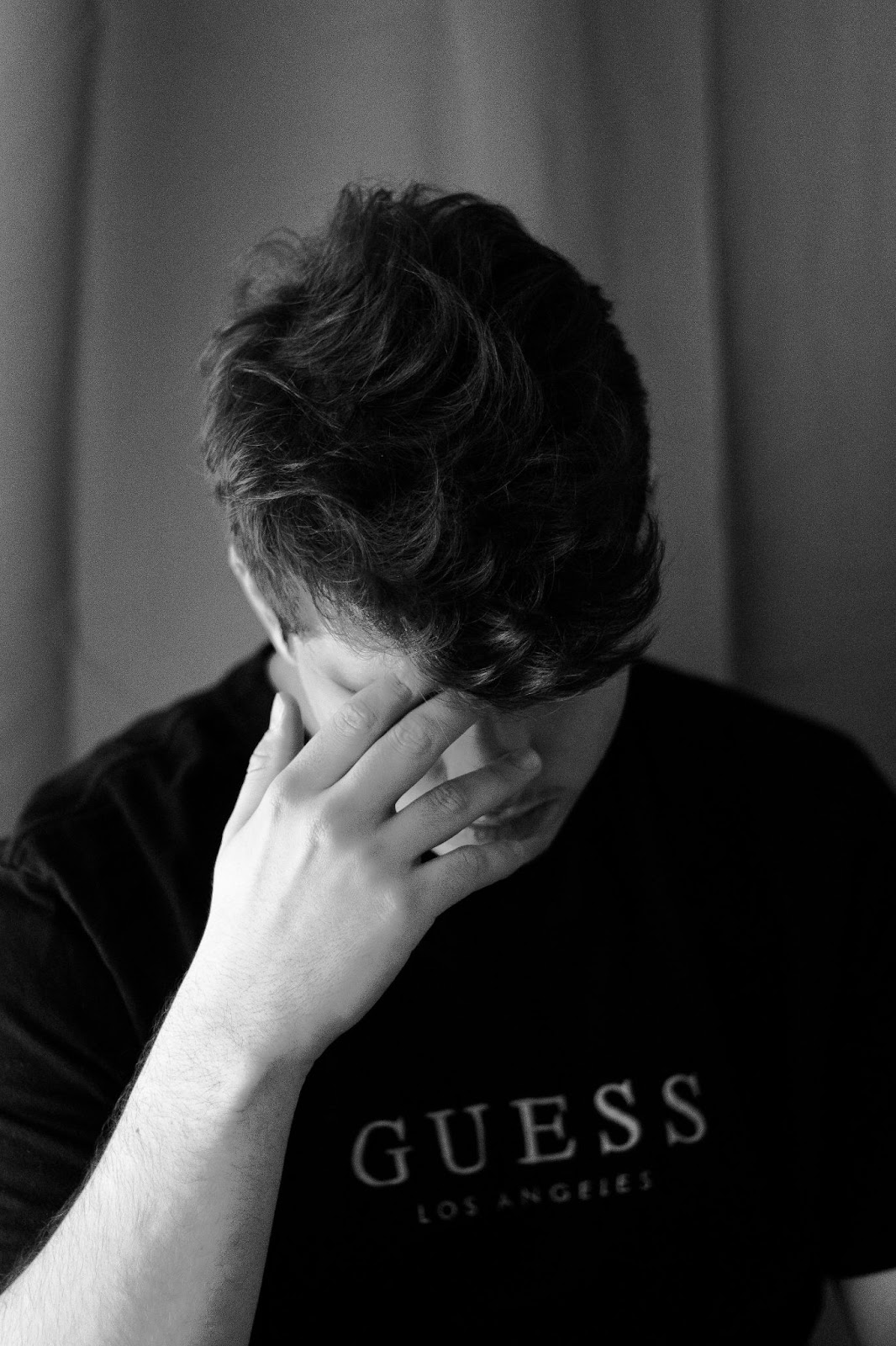 A picture of man, head bowed, looking downtrodden with the word Guess on his T-shirt.