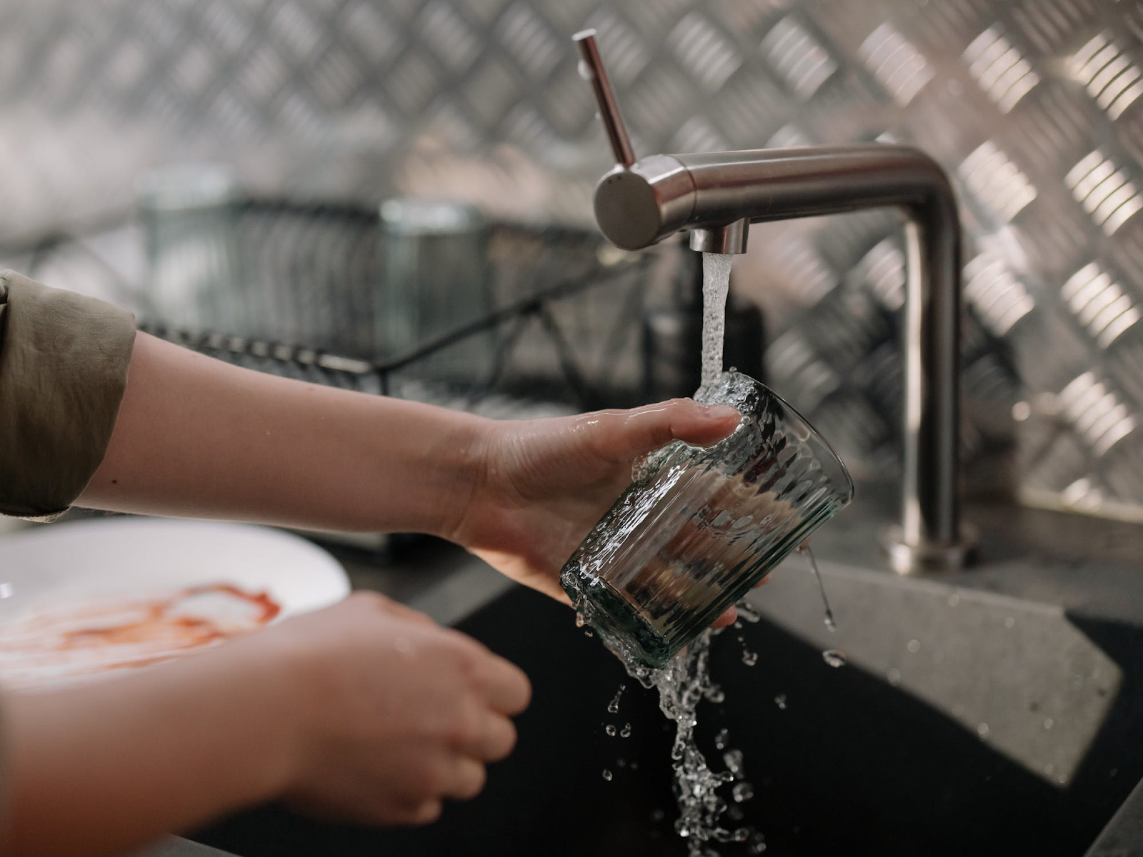 ženské ruky umývajú sklený pohár v prúde vody z nerezového kohútika