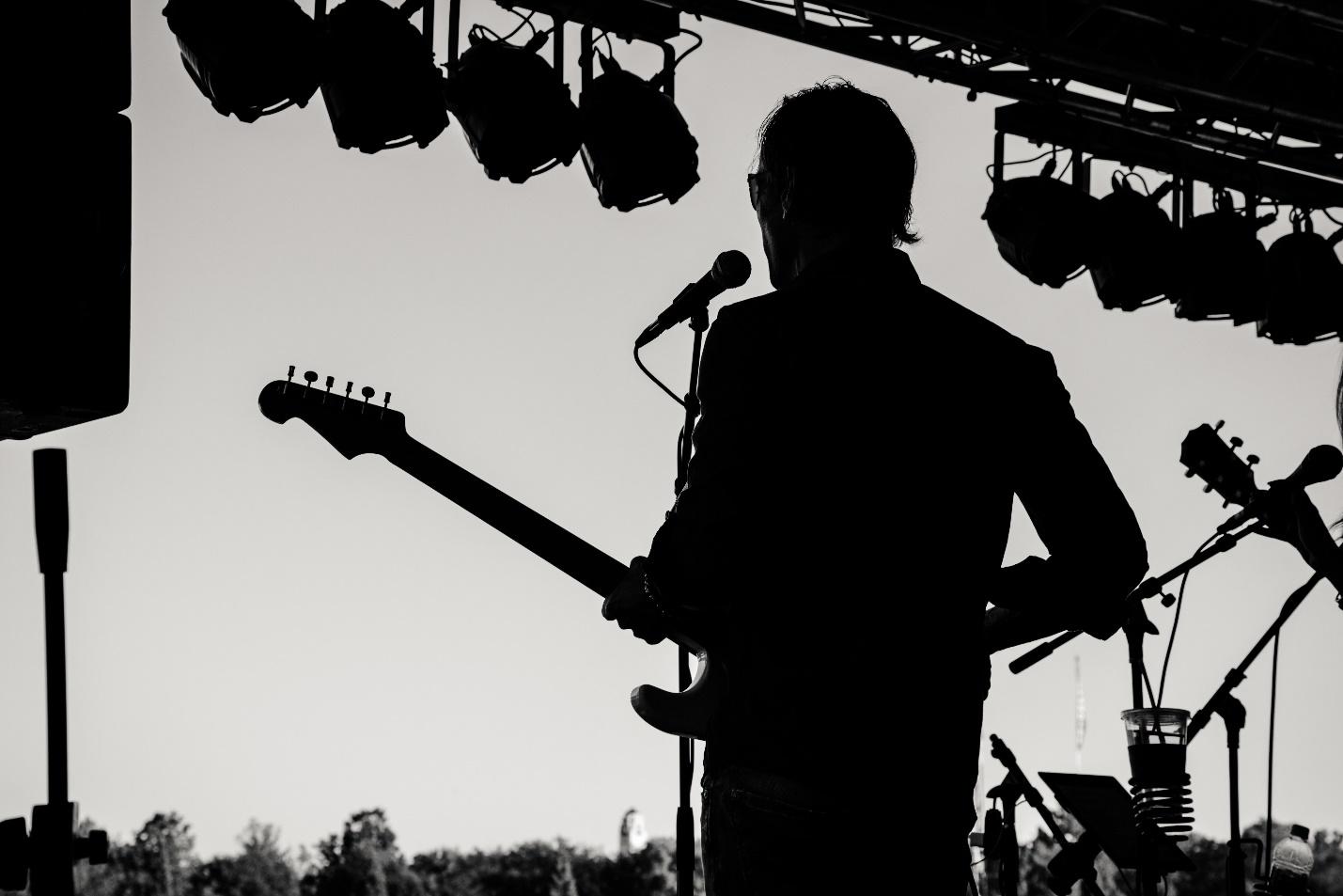 Silhouette photo of a man in front of a mic holding a guitar: Get A Gig As A Musician 