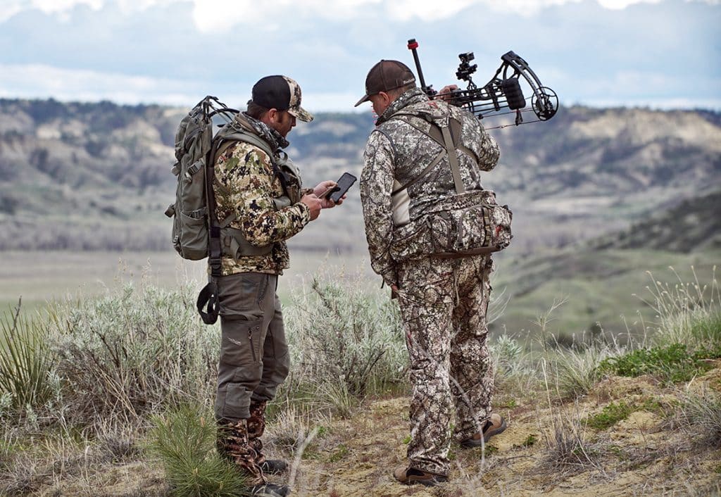 Two hunters look at a mobile phone while bowhunting in the mountains.
